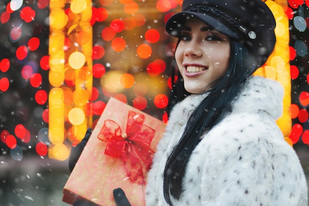 Elegante junge Frau, die während des Schneefalls ein Geschenk an der Feiertagsmesse erhält. Freiraum