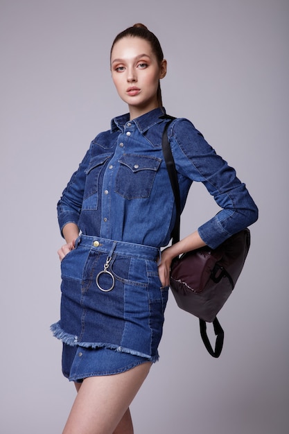 Elegante junge Frau in Denimjeans kleiden schwarze Turnschuhe braunen Rucksackstudiohintergrund