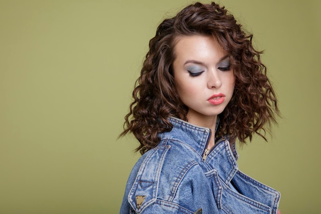 elegante junge frau in jeansjacke, blaue hose, weiße stiefel, posiert auf grünem hintergrund