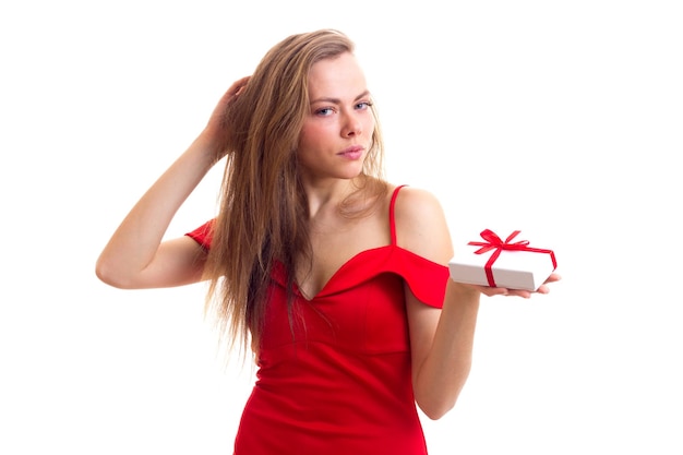 Elegante junge Frau mit langen braunen Haaren in einem knappen roten Kleid mit schwarzen Ohrringen, die ein Geschenk halten