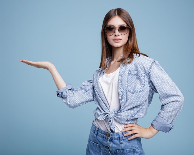 elegante junge glückliche frau in einem hübschen jeansrock, hemd, weißer oberseite, die auf blauem hintergrund aufwirft