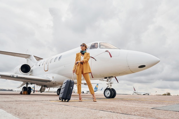 Elegante Kleidung Junge Frau mit Gepäck ist im Freien in der Nähe des Flugzeugs