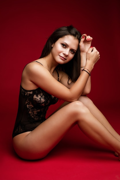 Elegante lencería negra en modelo de mujer joven en forma sentada sobre fondo rojo de estudio, espacio de copia para publicidad de ropa interior. Foto de alta calidad