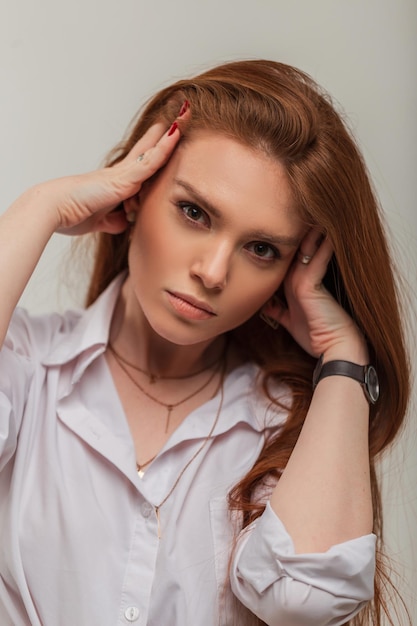 Elegante linda garota ruiva com um rosto bonito em uma camisa branca da moda em um fundo branco