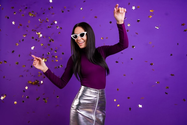 Foto elegante linda mujer bailando en la caída de confeti asistiendo a un club nocturno aislado color vibrante pared púrpura