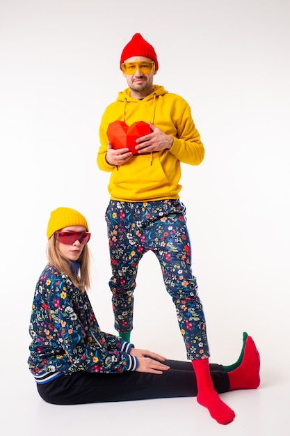 Elegante linda pareja de hombre y mujer en ropa colorida posando con corazón sobre pared blanca