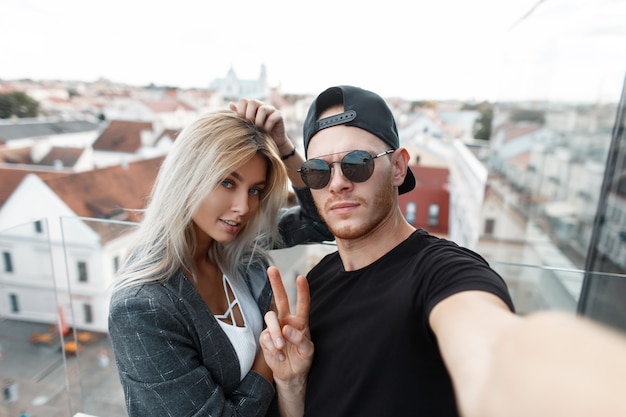 Elegante lindo casal jovem fazendo selfie na cidade. homem moderno com uma mulher elegante viaja e tira fotos