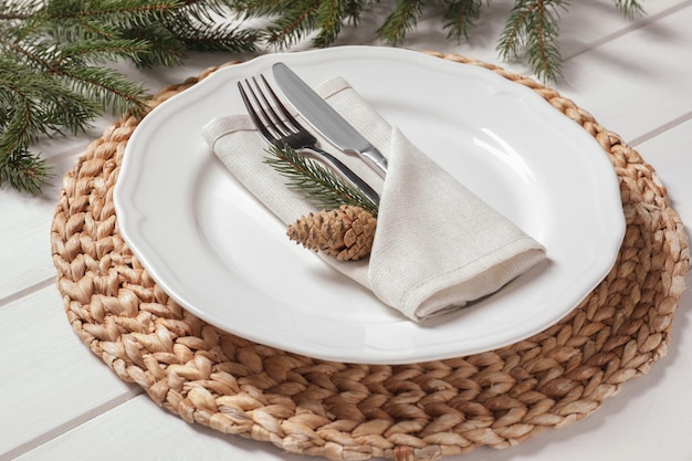 Elegante lugar festivo con cubiertos y ramas de abeto en el primer plano de la mesa de madera blanca