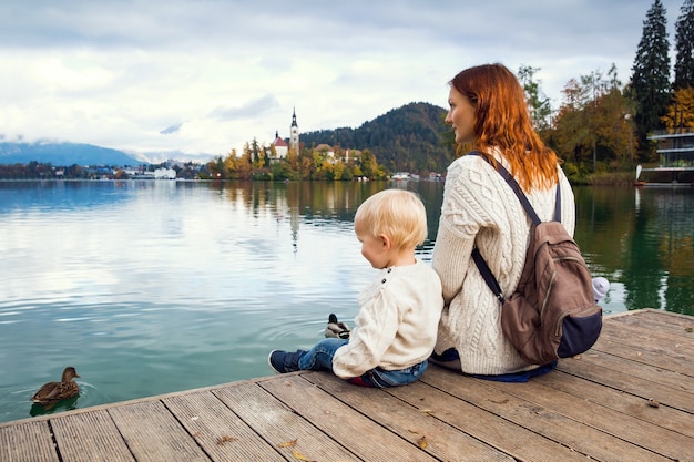 Elegante madre e hijo sentados en un muelle de madera en el lago Bled, Eslovenia