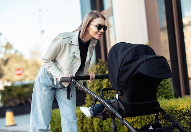 Elegante mamá amorosa camina con un cochecito en la ubicación de la ciudad Estilo de vida de maternidad