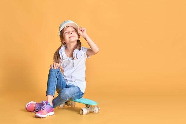 Elegante menina criança menina casual com skate na parede amarela