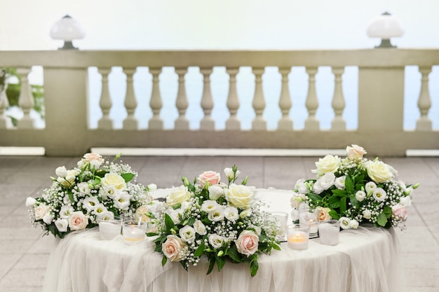 Elegante mesa de boda al aire libre con tres ramilletes de flores rosas y blancas y velas en un patio al aire libre con balaustrada