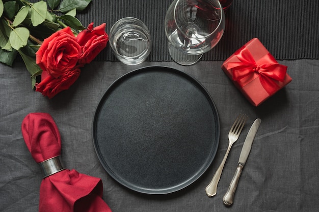 Elegante mesa con rosa roja sobre mantel de lino negro.