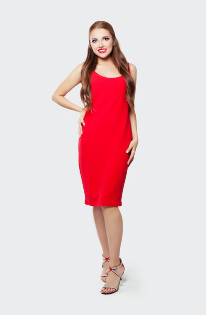 Elegante Modelfrau mit rotem Kleid und hohen Absätzen steht vor einem weißen Wandhintergrund