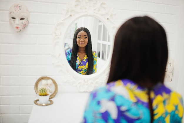 Elegante modelo de mujer afroamericana vestida con ropa de colores Mujeres afro elegantes en la habitación mirando al espejo