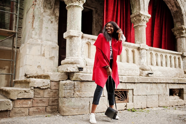 Elegante mujer con abrigo rojo posando contra columnas antiguas