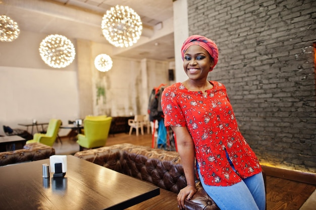 Elegante mujer africana con camisa roja y sombrero posó en un café interior