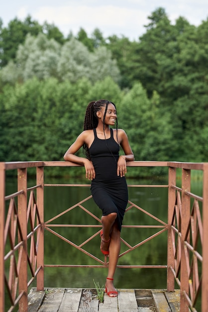 Foto elegante mujer afro en traje de moda se encuentra cerca de un lago azul en un día soleado de verano