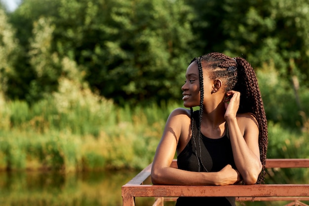 Elegante mujer afro en traje de moda se encuentra cerca de un lago azul en un día soleado de verano