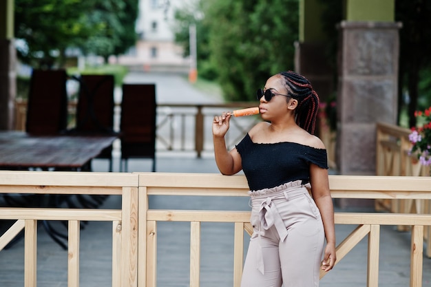 Elegante mujer afroamericana en gafas de sol con helado