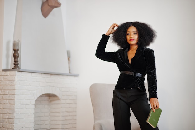 Foto elegante mujer afroamericana en negro posó en la habitación contra chimenea leer libros.