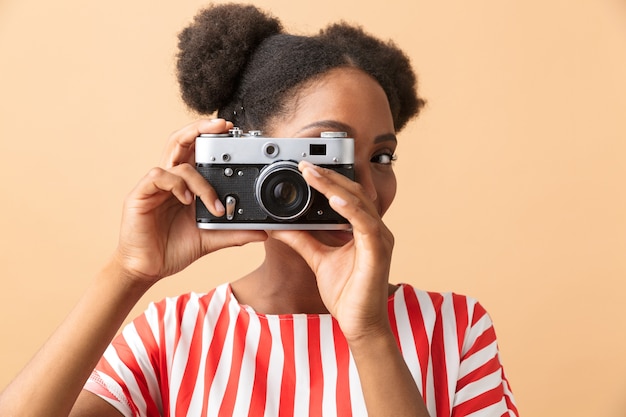 Elegante mujer afroamericana sonriendo y fotografiando en cámara retro, aislada