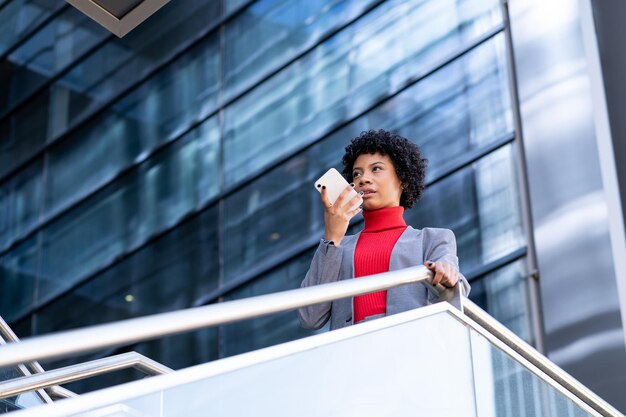 Una elegante mujer afroamericana usando el teléfono en un edificio de oficinas en el trabajo