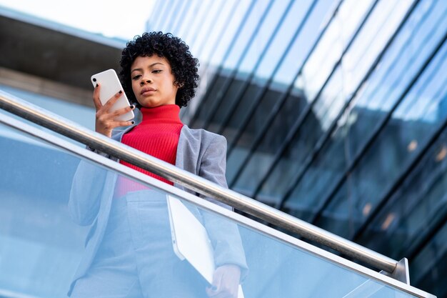Una elegante mujer afroamericana usando el teléfono en un edificio de oficinas en el trabajo