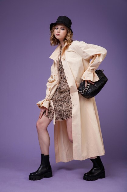 Elegante mujer en beige crema trench coat vestido marrón con un patrón floral sombrero negro botas bolso