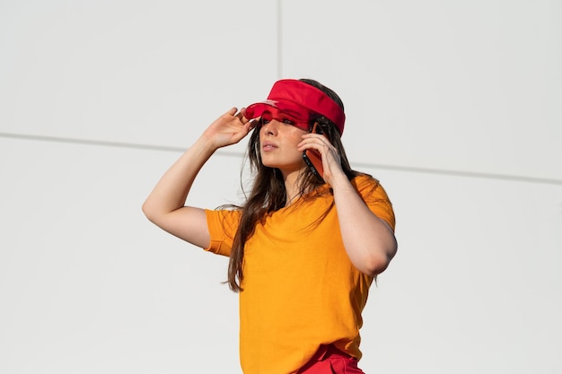 Foto elegante mujer caucásica con una camiseta naranja y una gorra roja hablando por teléfono