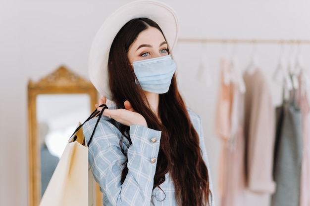 Elegante mujer caucásica en máscara protectora con bolsa de compras en boutique de moda mientras compra