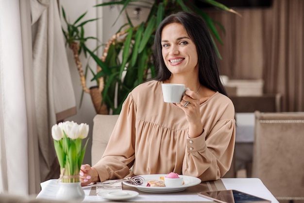 Elegante mujer caucásica vestida está comiendo un sabroso postre dulce en la cafetería