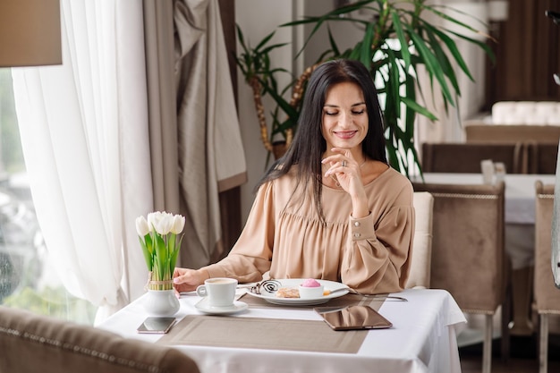 Elegante mujer caucásica vestida está comiendo un sabroso postre dulce en la cafetería