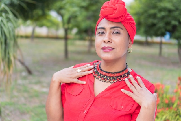 Elegante mujer étnica en ropa ornamental frente a la cámara con un turbante en el parque Mujer afro mirando hacia un lado con un turbante en el parque