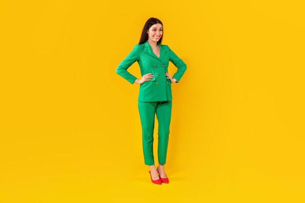 Elegante mujer feliz con traje verde mirando a un lado y sonriendo fondo amarillo de cuerpo entero gratis