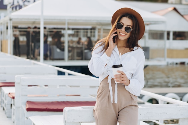 Una elegante mujer hablando por teléfono y caminando por la playa en un cálido día de verano al atardecer