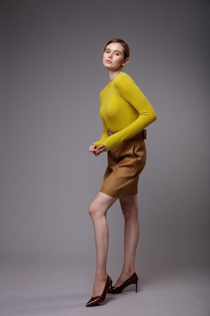 Elegante mujer joven en una bonita falda de arena beige marrón suéter amarillo mostaza sobre fondo gris