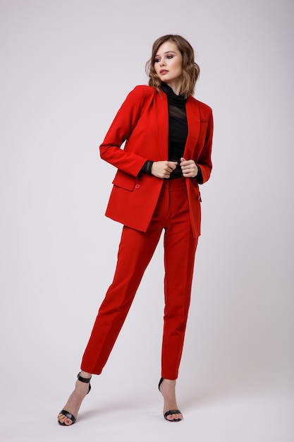 Elegante mujer joven en un bonito traje rojo chaqueta pantalones pantalones blusa negra sobre fondo blanco.