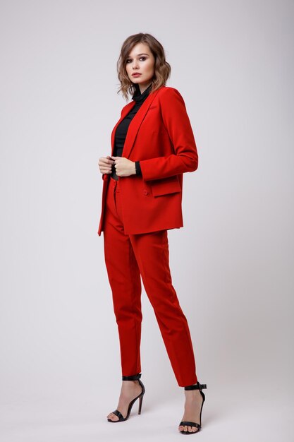 Elegante mujer joven en un bonito traje rojo chaqueta pantalones pantalones blusa negra sobre fondo blanco.