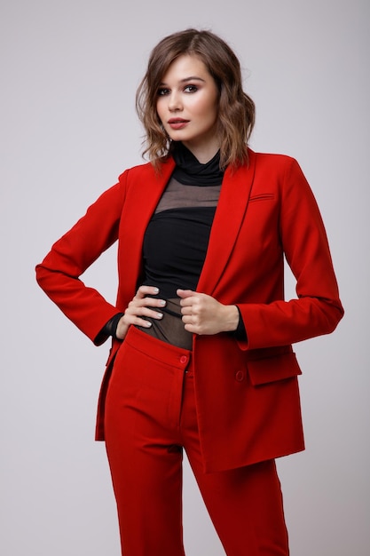 Elegante mujer joven en un bonito traje rojo chaqueta pantalones pantalones blusa negra sobre fondo blanco.