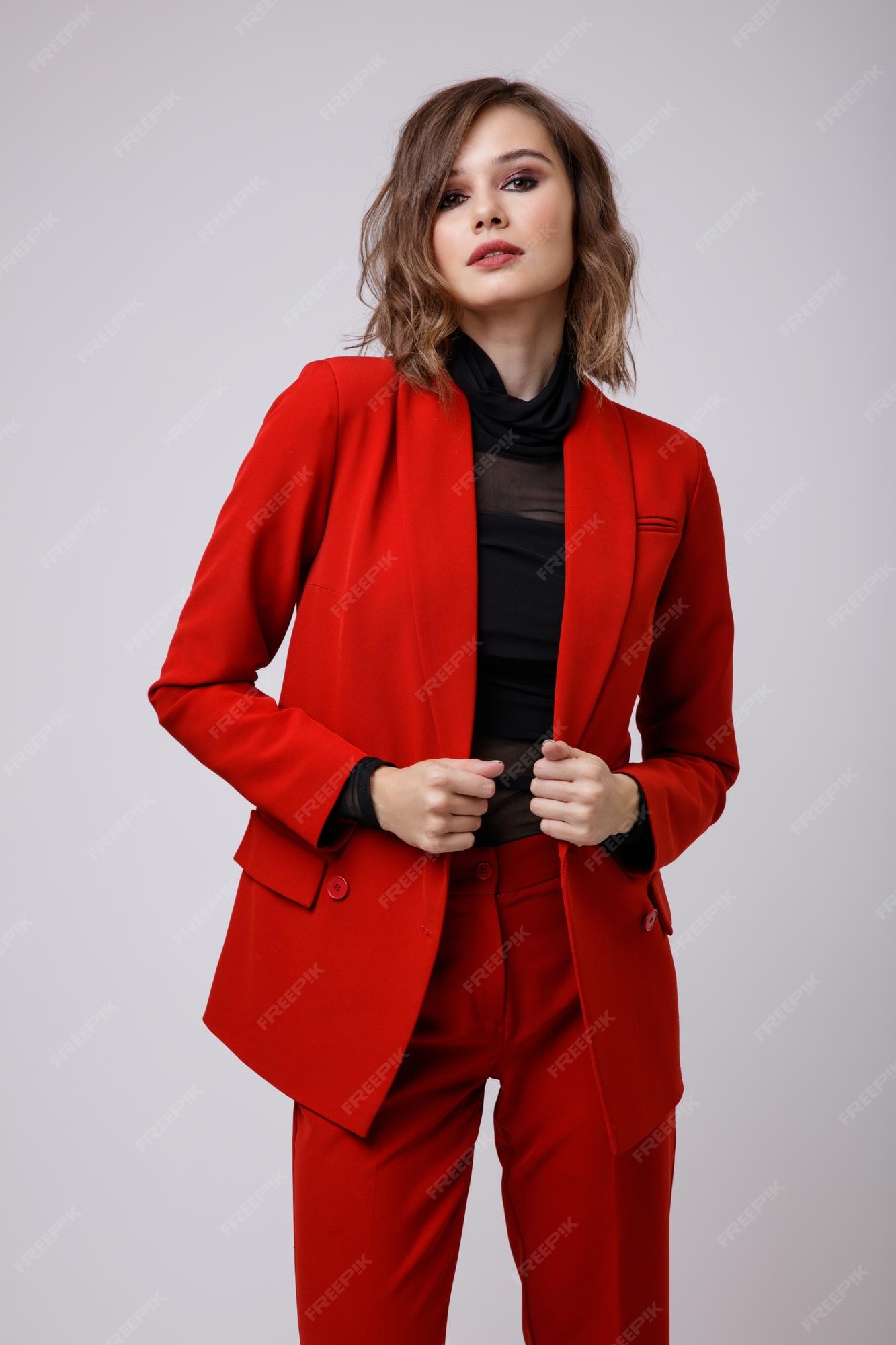 Elegante mujer joven en un bonito traje rojo chaqueta pantalones blusa negra sobre fondo blanco. | Foto Premium