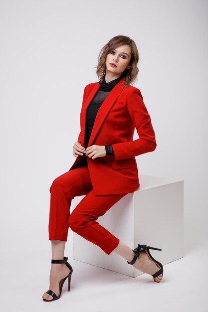 Elegante mujer joven en un bonito traje rojo chaqueta pantalones pantalones blusa negra sobre fondo blanco.