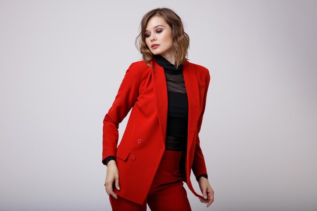 Elegante mujer joven en un bonito traje rojo chaqueta pantalones pantalones blusa negra sobre fondo blanco.