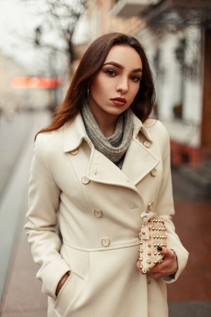 Elegante mujer joven moderna con un abrigo de moda con un elegante bolso de moda el día de invierno en la ciudad