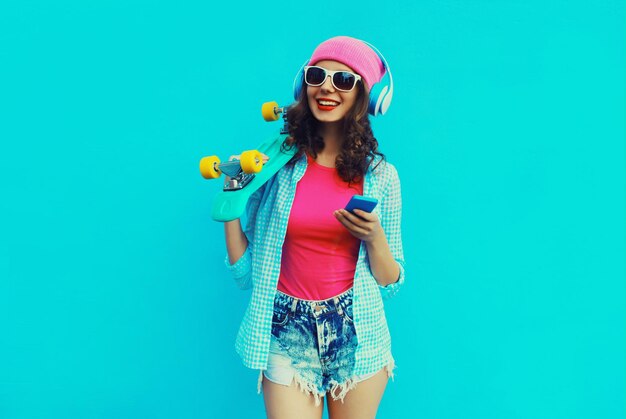 Foto elegante mujer joven moderna feliz escuchando música en auriculares con skateboard de teléfono inteligente