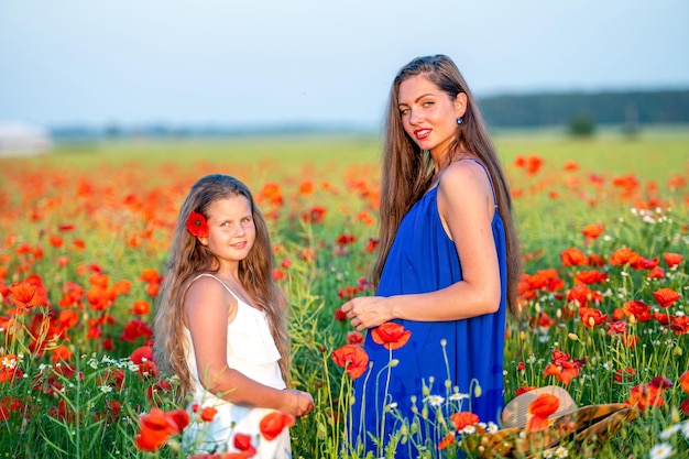 Elegante mujer joven con niña en el campo de amapolas familia feliz divirtiéndose en la naturaleza el horario de verano