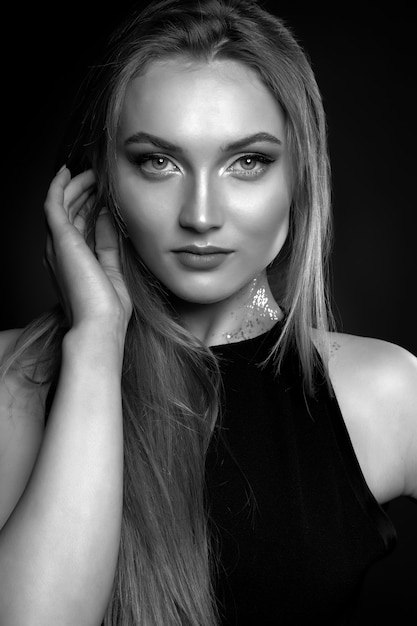 Elegante mujer joven con pelo largo y liso viste un vestido negro clásico posando a la sombra en el estudio. Disparo en blanco y negro