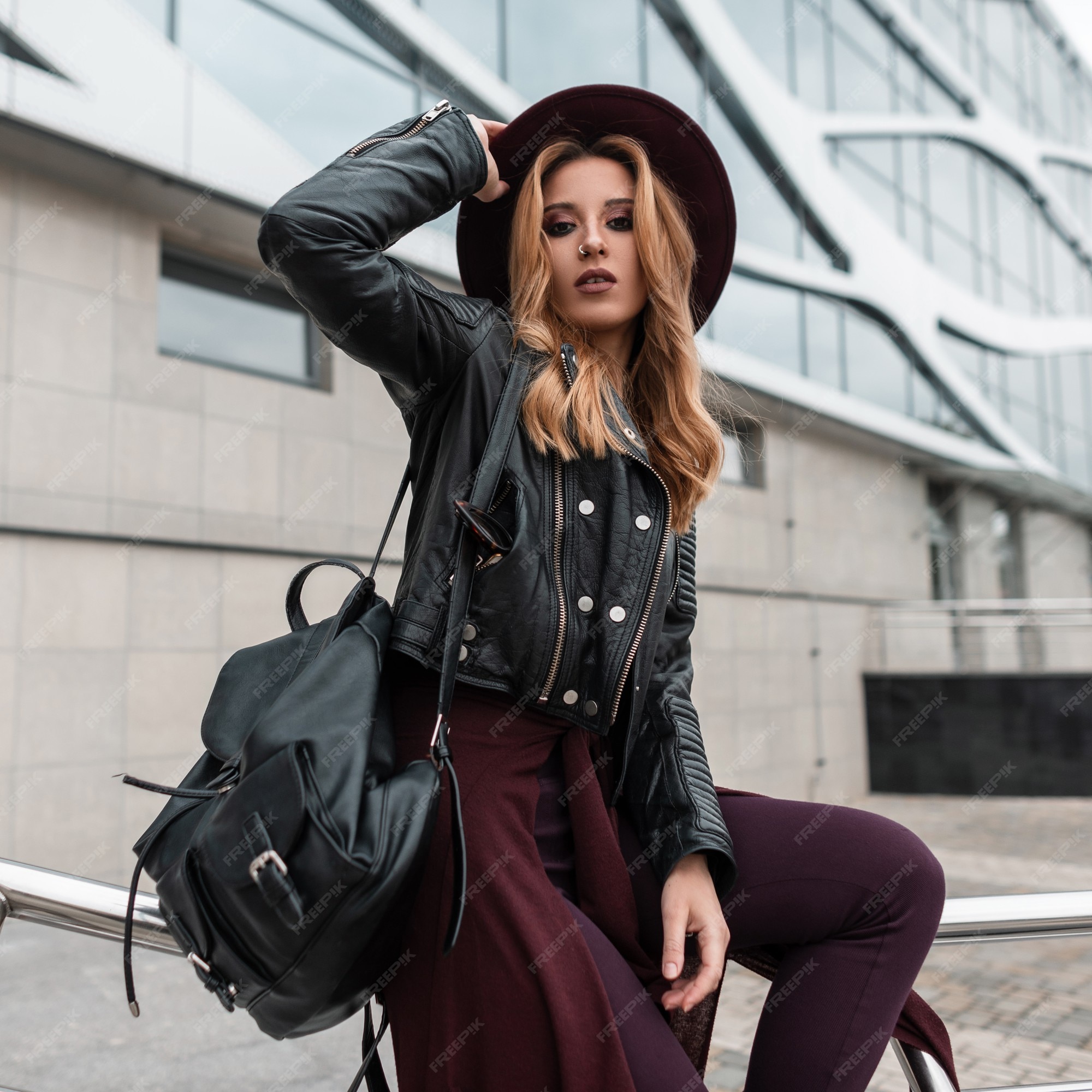 Elegante mujer joven con pelo rojo en una chaqueta negra una mochila de cuero en pantalones de moda | Foto