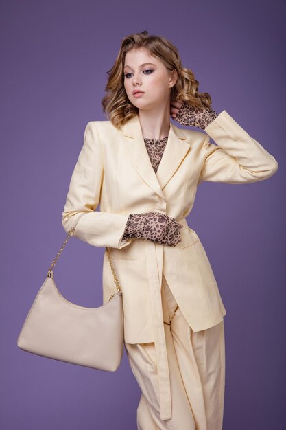 Elegante mujer joven en traje de lino crema beige chaqueta pantalones blazer handbad sobre fondo púrpura