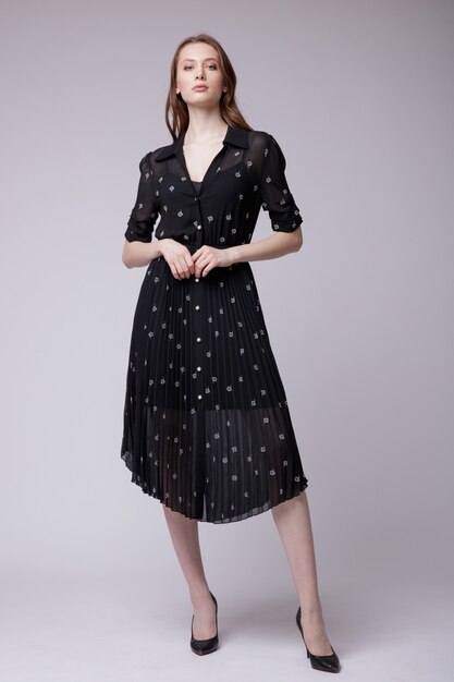 Elegante mujer joven en vestido negro con pequeñas flores blancas sobre fondo blanco Foto de estudio